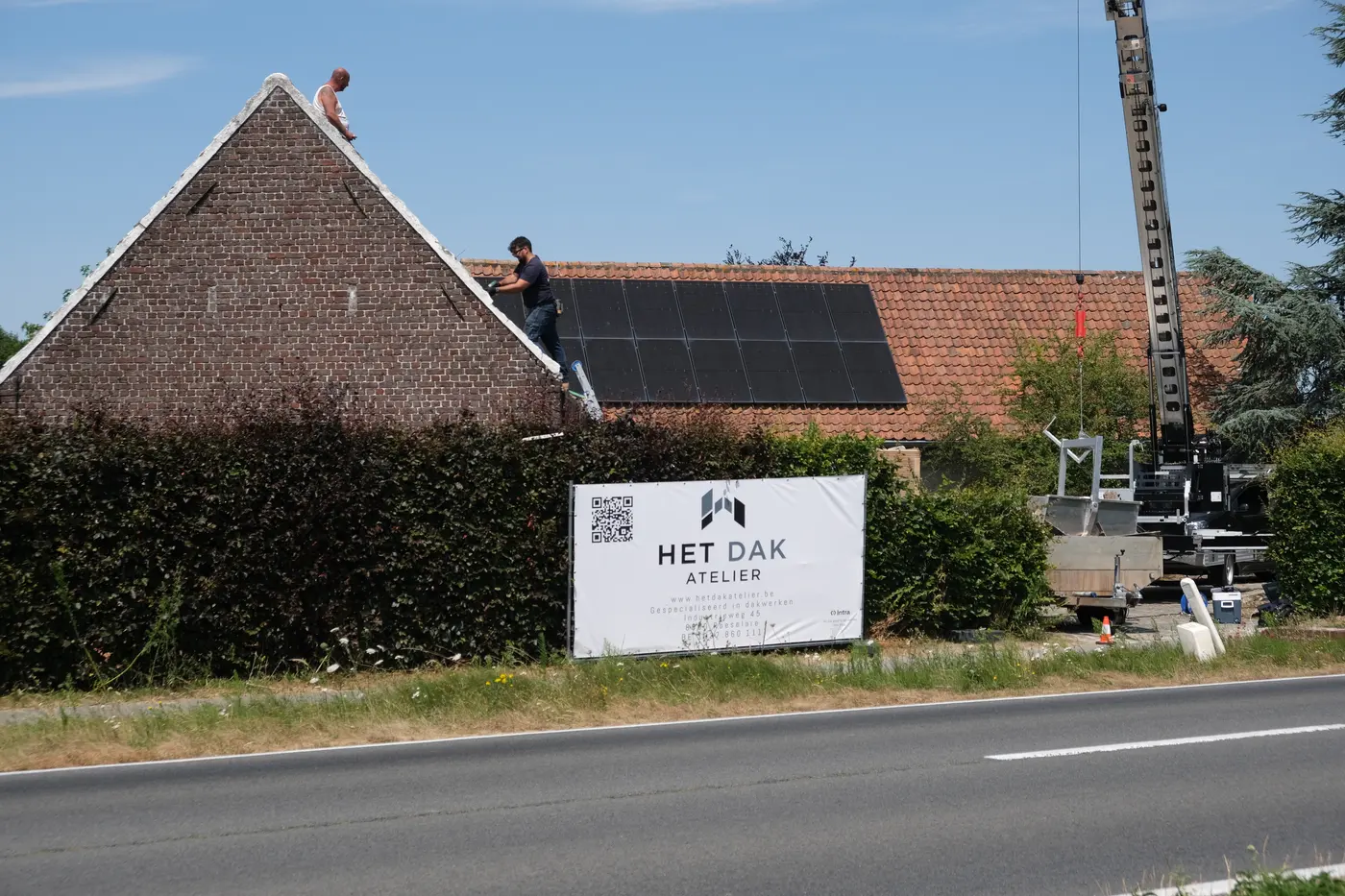 Werf van Het Dak Atelier in Aalter — team aan het werk op het dak, met werfdoek aan de straat
